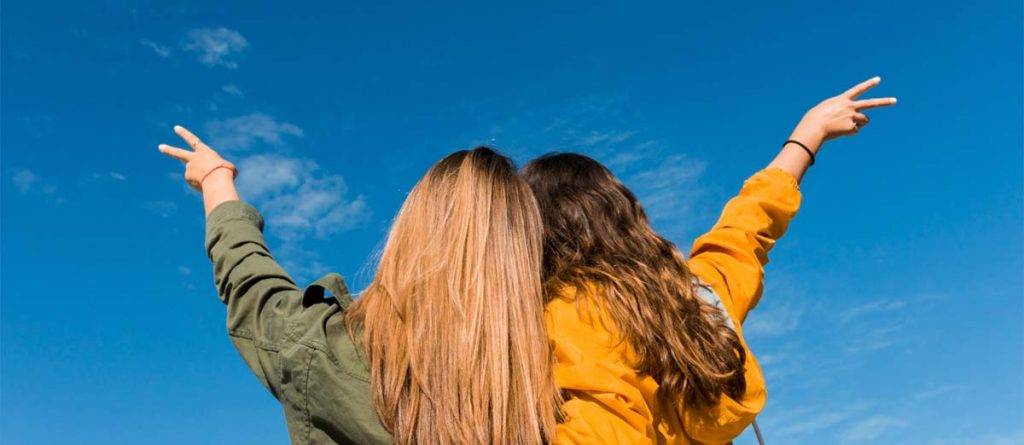 Imagen de dos mujeres jóvenes celebrando bajo un cielo azul