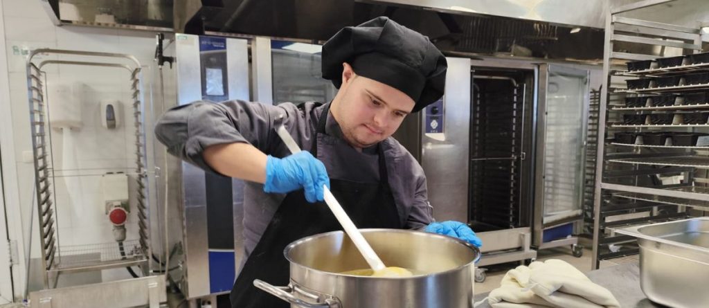David, ayudante de cocina de la Fundación AMÁS removiendo un cucharón en una olla.